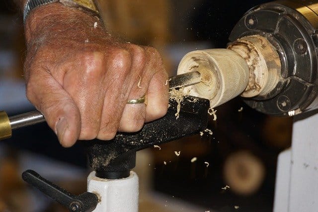 A man's hand chiseling into wood on a lathe