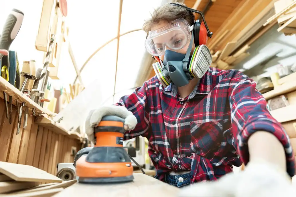 professional female carpenter grinding raw wood with orbital sander
