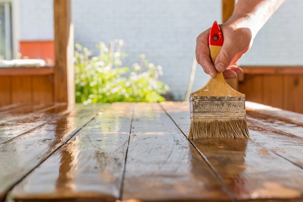 Hand-with-a-brush-varnishes-a-wooden-table-in-a-gazebo-closeup
