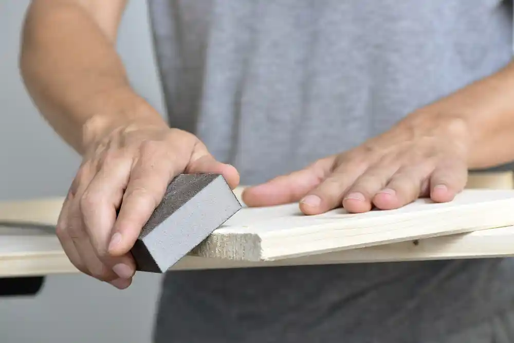 closeup of a young caucasian man sanding a wooden board with a sanding block